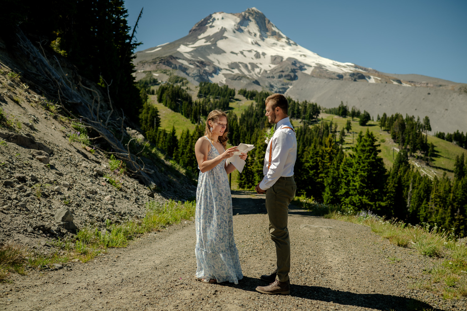 A couple stands on a mountain path at Mt Hood Meadows, exchanging vows during their elopement against a backdrop of the snow-capped peaks of Mt Hood.