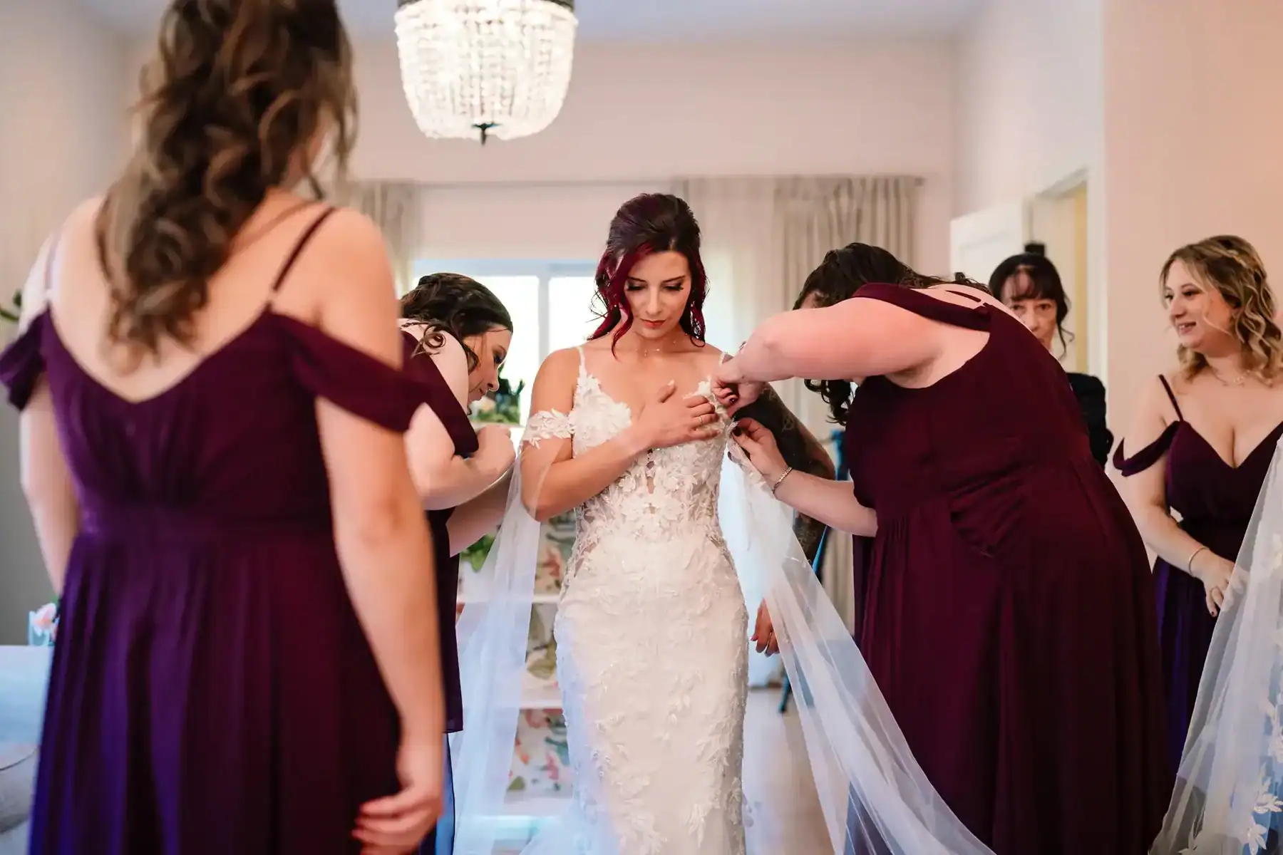 Bride surrounded by bridesmaids helping her with her dress before the ceremony, captured candidly by Ladman Studios in Connecticut.