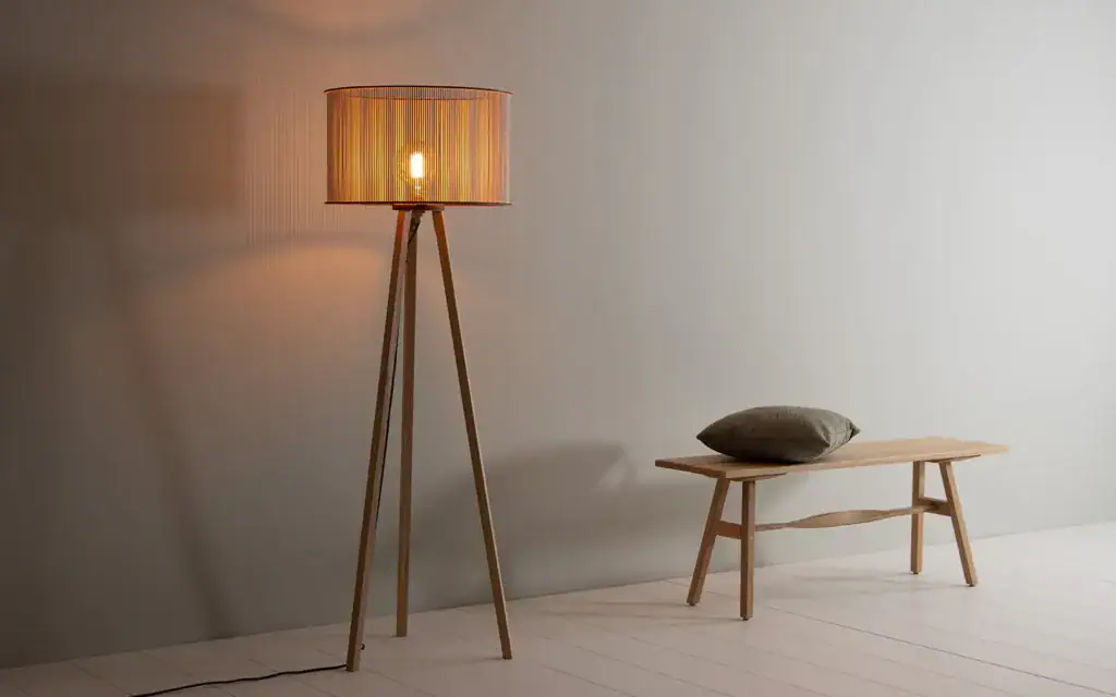 Elegant wooden tripod floor lamp with warm light in minimalist space.