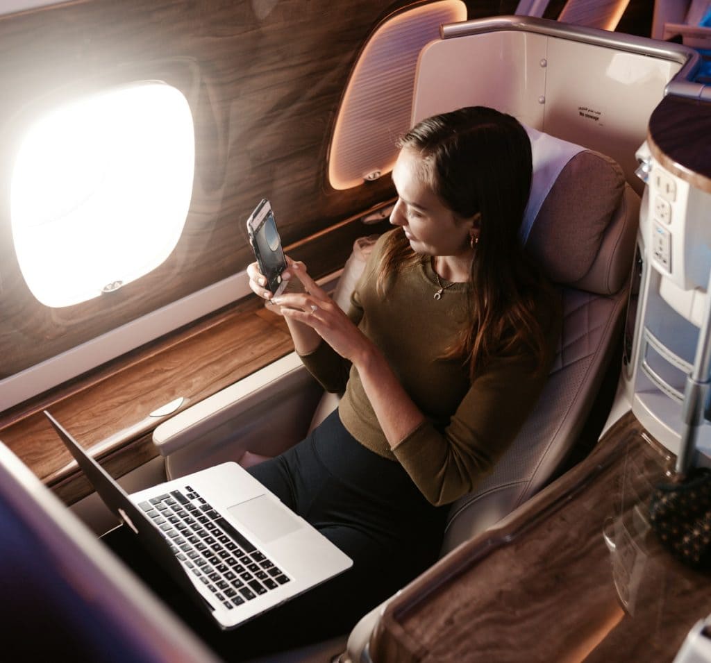 Business traveller using a phone and laptop in a business-class airline seat