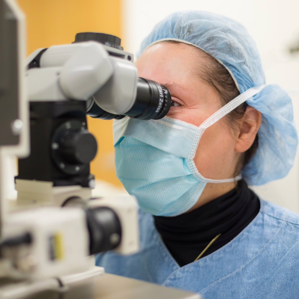 Person in medical attire looking into a microscope