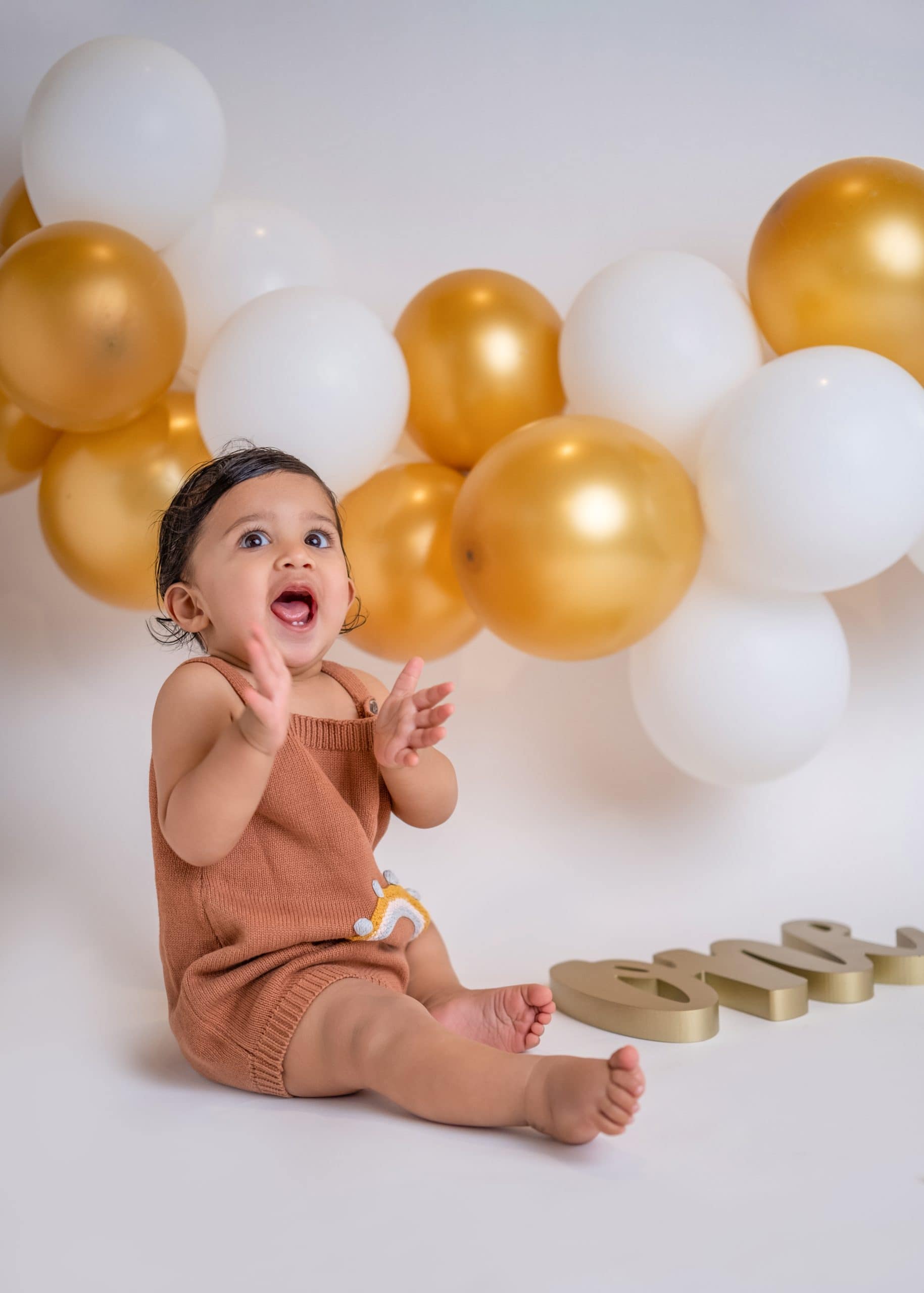 Minimalist cake smash photo with golden balloons, and a clean background in an Edmonton studio.