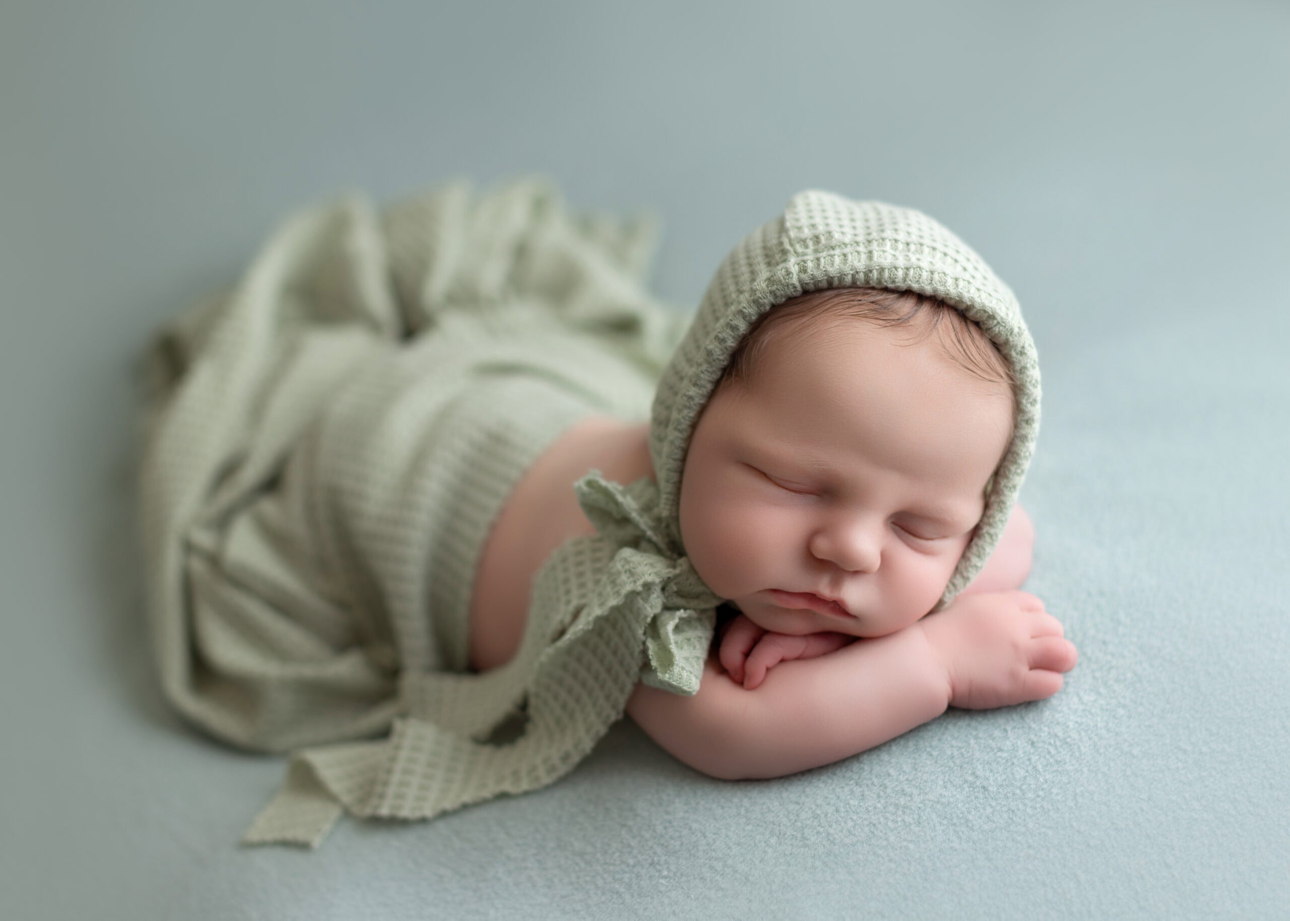 newborn baby boy taking his newborn photo in soft green sage colour with little one photography