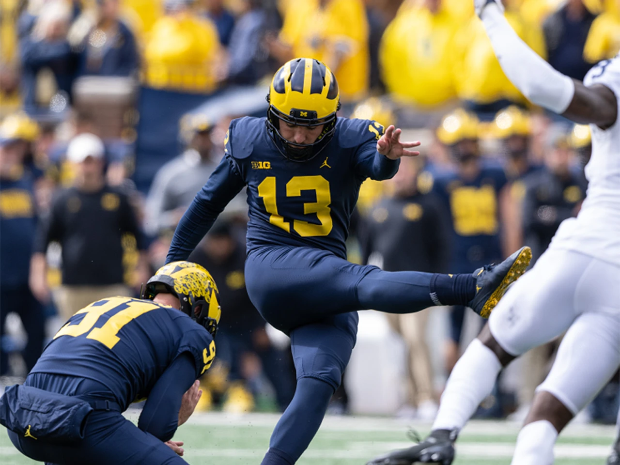 Michigan football player kicking a field goal during a game at Michigan Stadium.