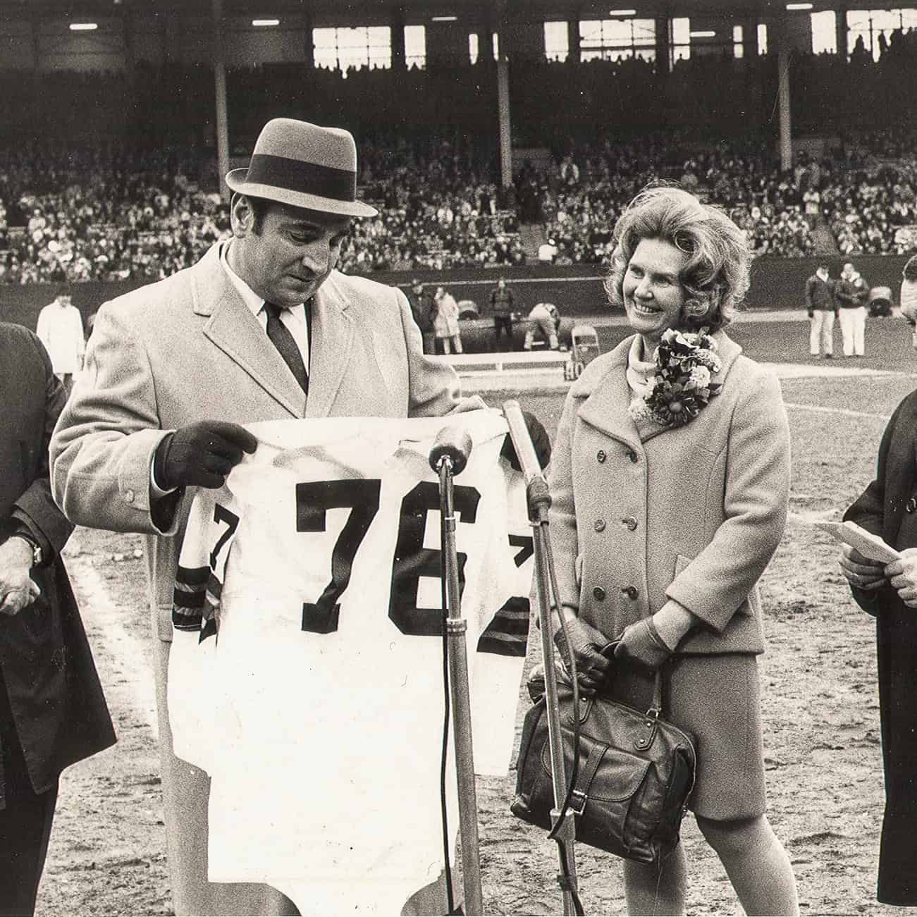 Historical black and white photo of a man and woman at a sports event, woman holding a purse.