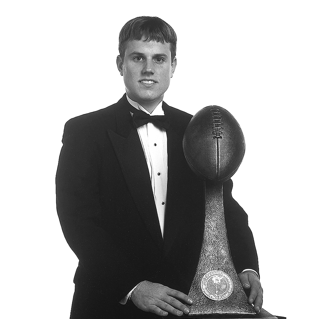 Young man in tuxedo holding Lou Groza Award trophy with football.
