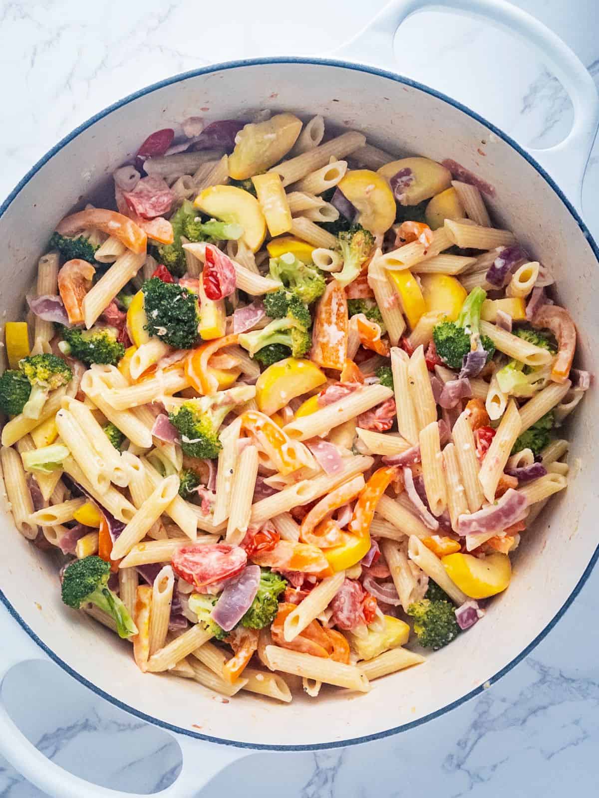 colorful sauteed vegetables and penne pasta in lemon cream sauce in a large white pot