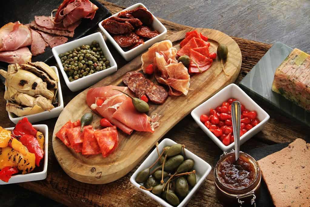 charcuterie board with meats and pâté with peppers, artichoke hearts, capers, sun-dried tomatoes, petit poivrons, and caperberries