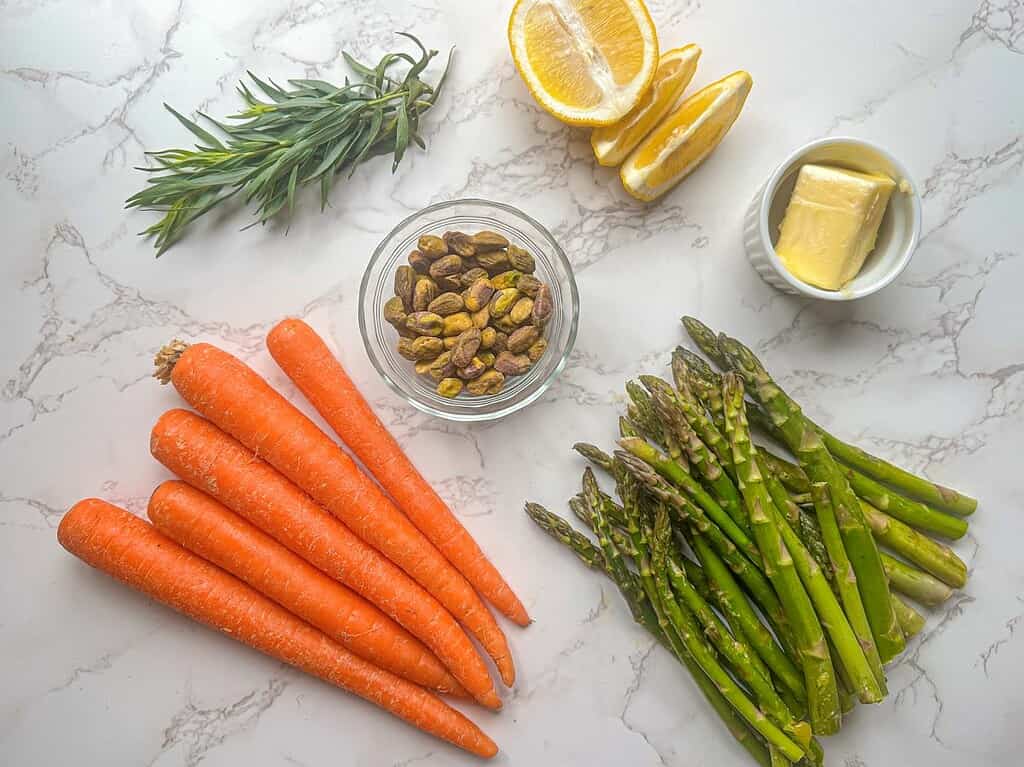 carrots, asparagus, pistachios, butter, lemon and fresh tarragon on marble countertop