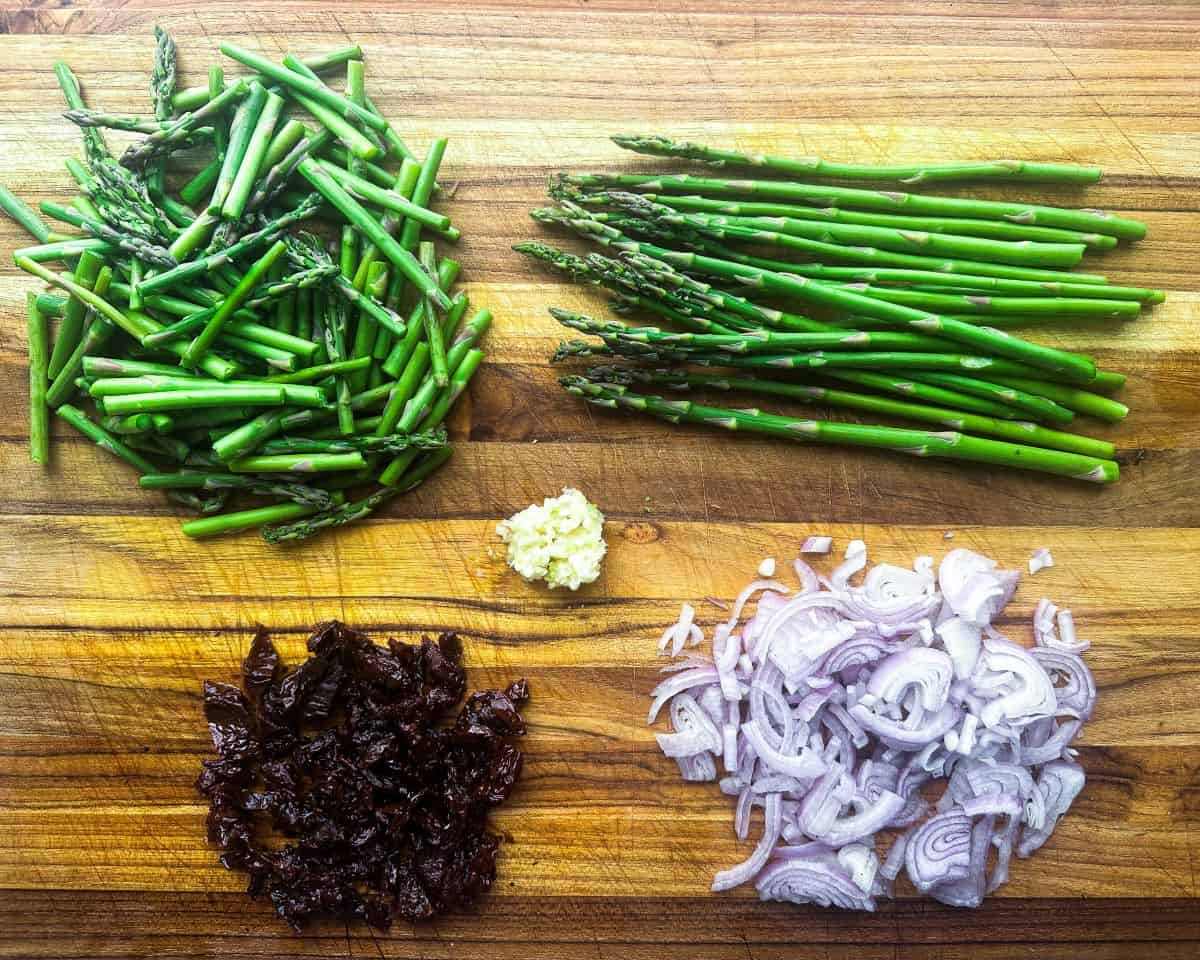 Chopped asparagus, sundried tomatoes, shallots and garlic on wood cutting board