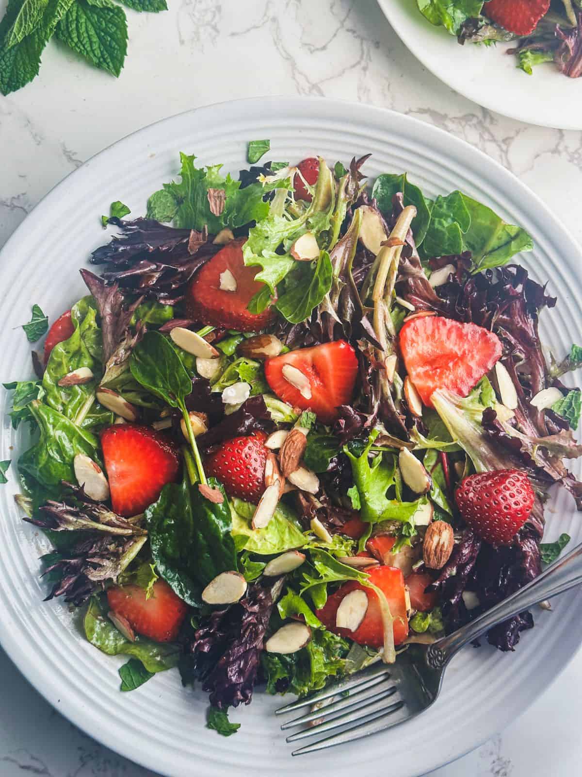Strawberries, spring mix greens, and toasted almonds in a large white bowl.