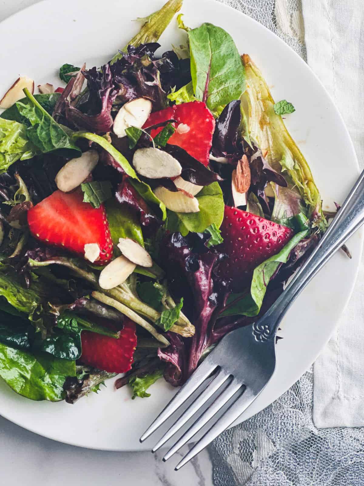 Close up shot of strawberry spring salad with a fork and lace napkin.