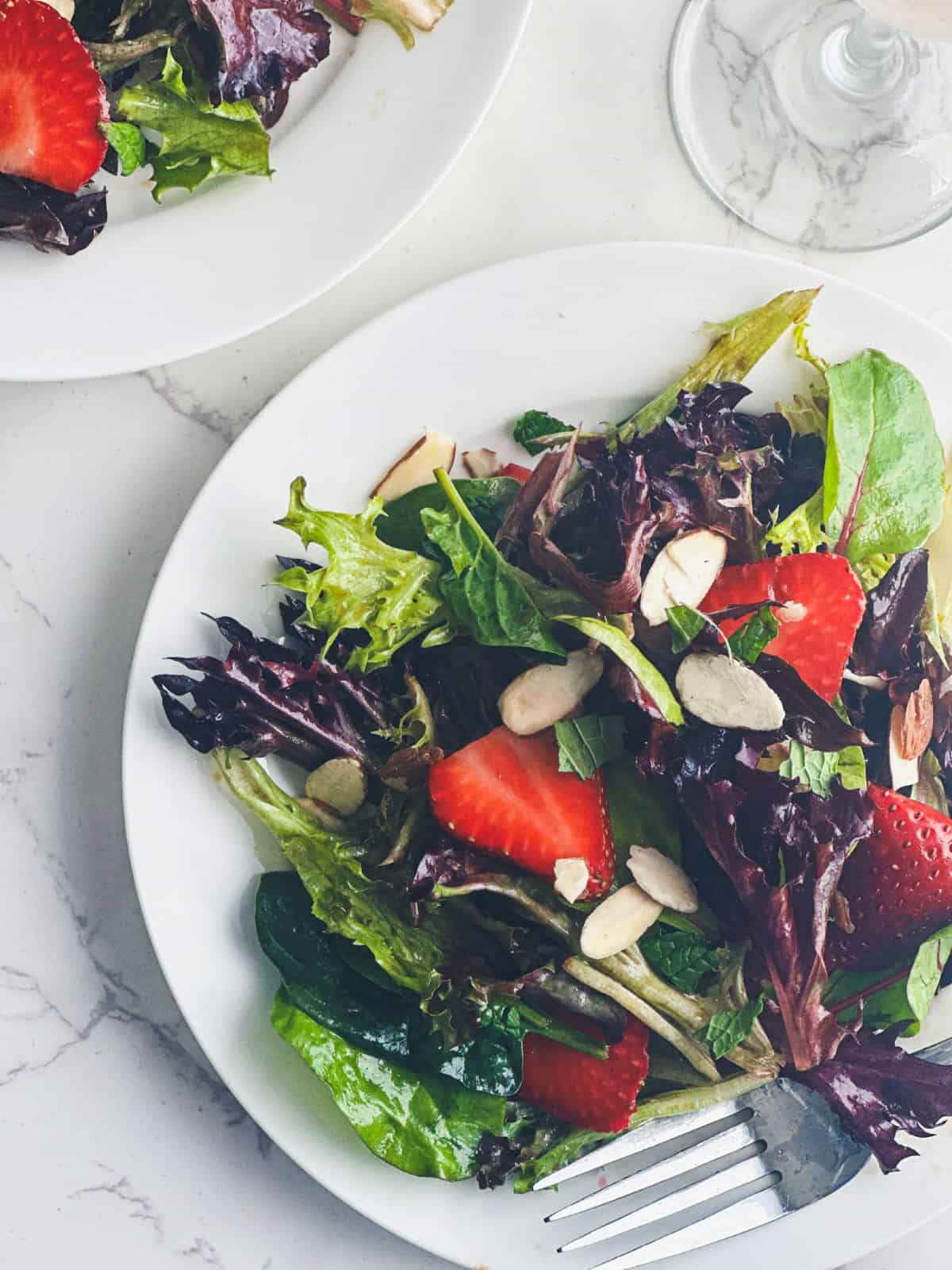 Strawberry spring mix salad with almonds on small plates.