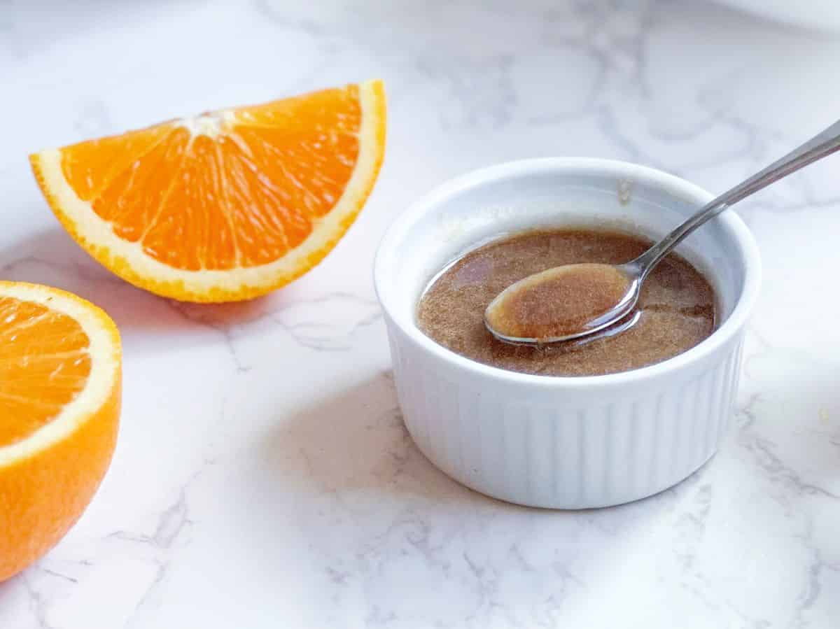 Balsamic citrus vinaigrette in a white ramekin with spoon and sliced oranges.