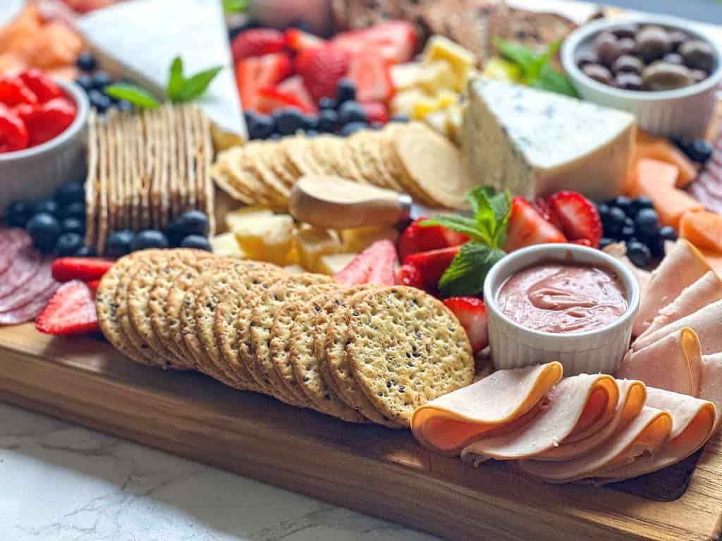 Charcuterie board with crackers, sauces, meats, and cheese.