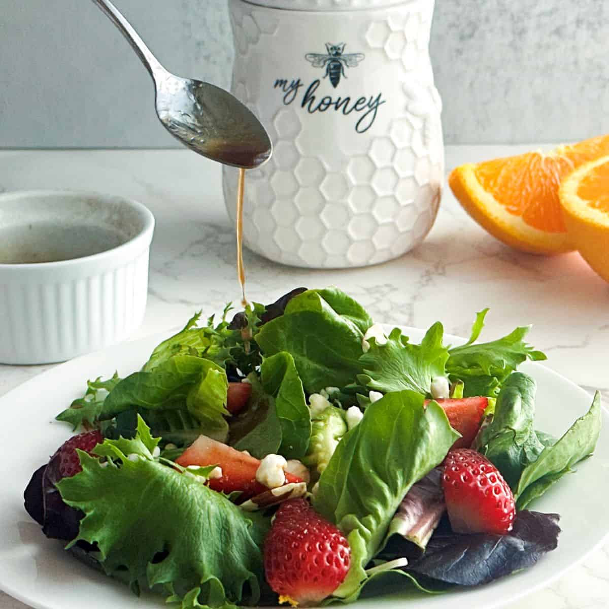 Strawberry spring salad with a spoon drizzling vinaigrette.