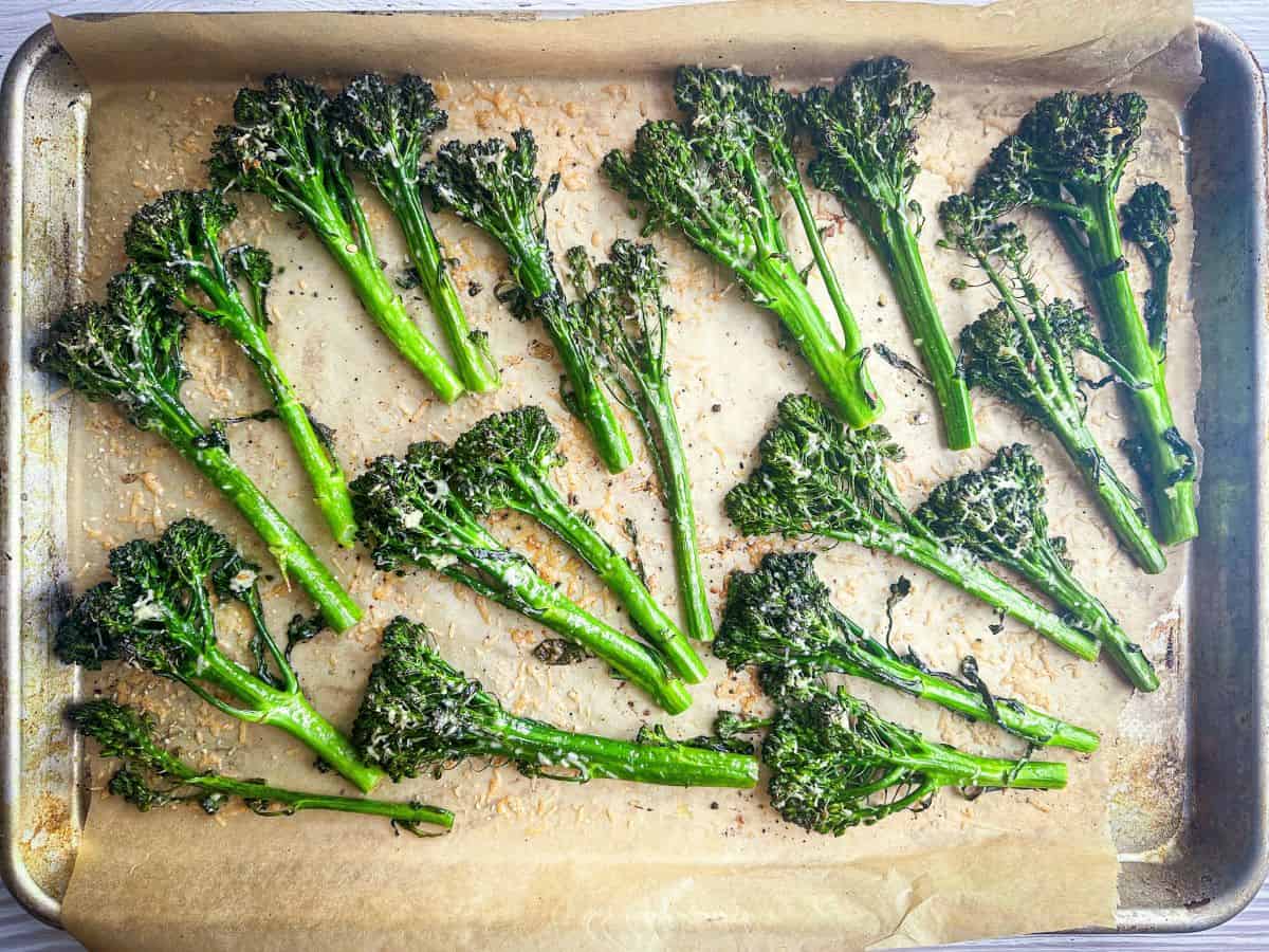 Charred broccolini with melted parmesan on a baking sheet with parchment paper.