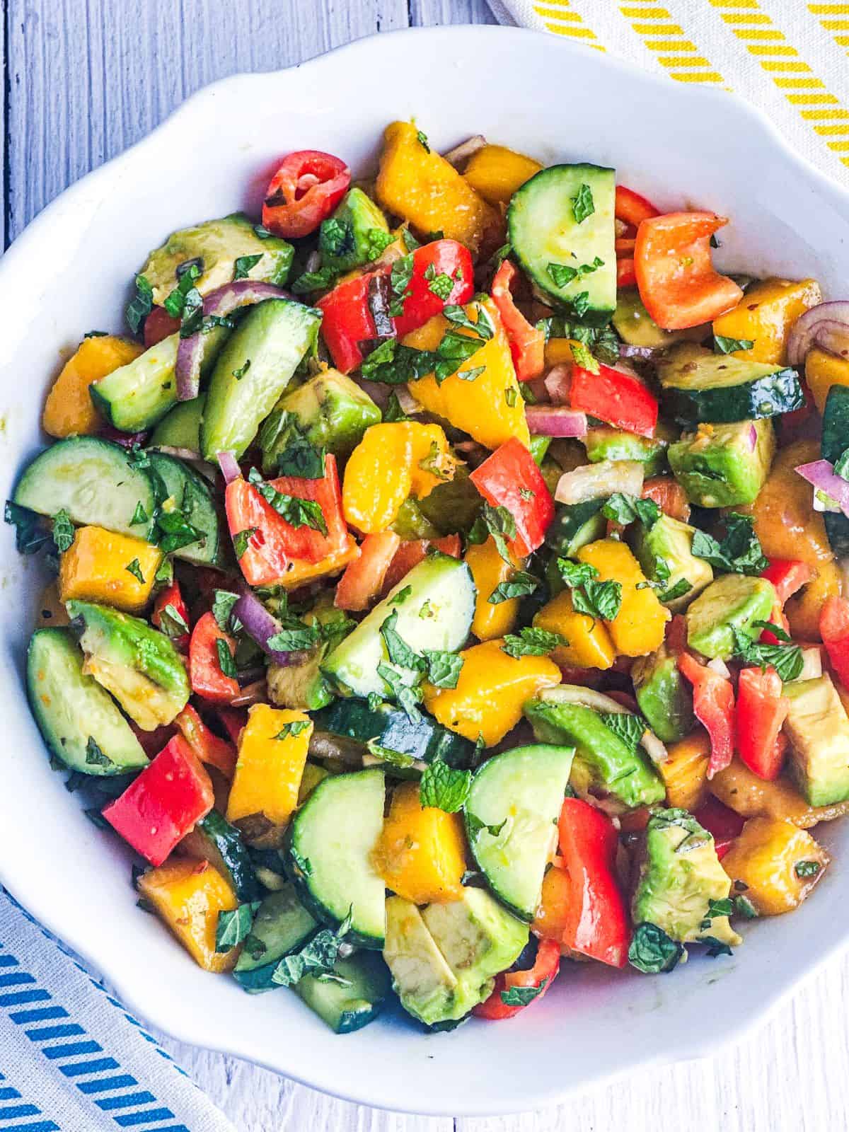 Mango, cucumber, and avocado salad with citrus vinaigrette in a white bowl with a spoon on the side.