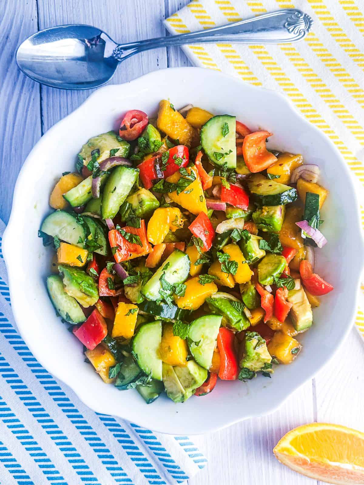 Mango cucumber avocado salad in a white bowl with orange wedge.