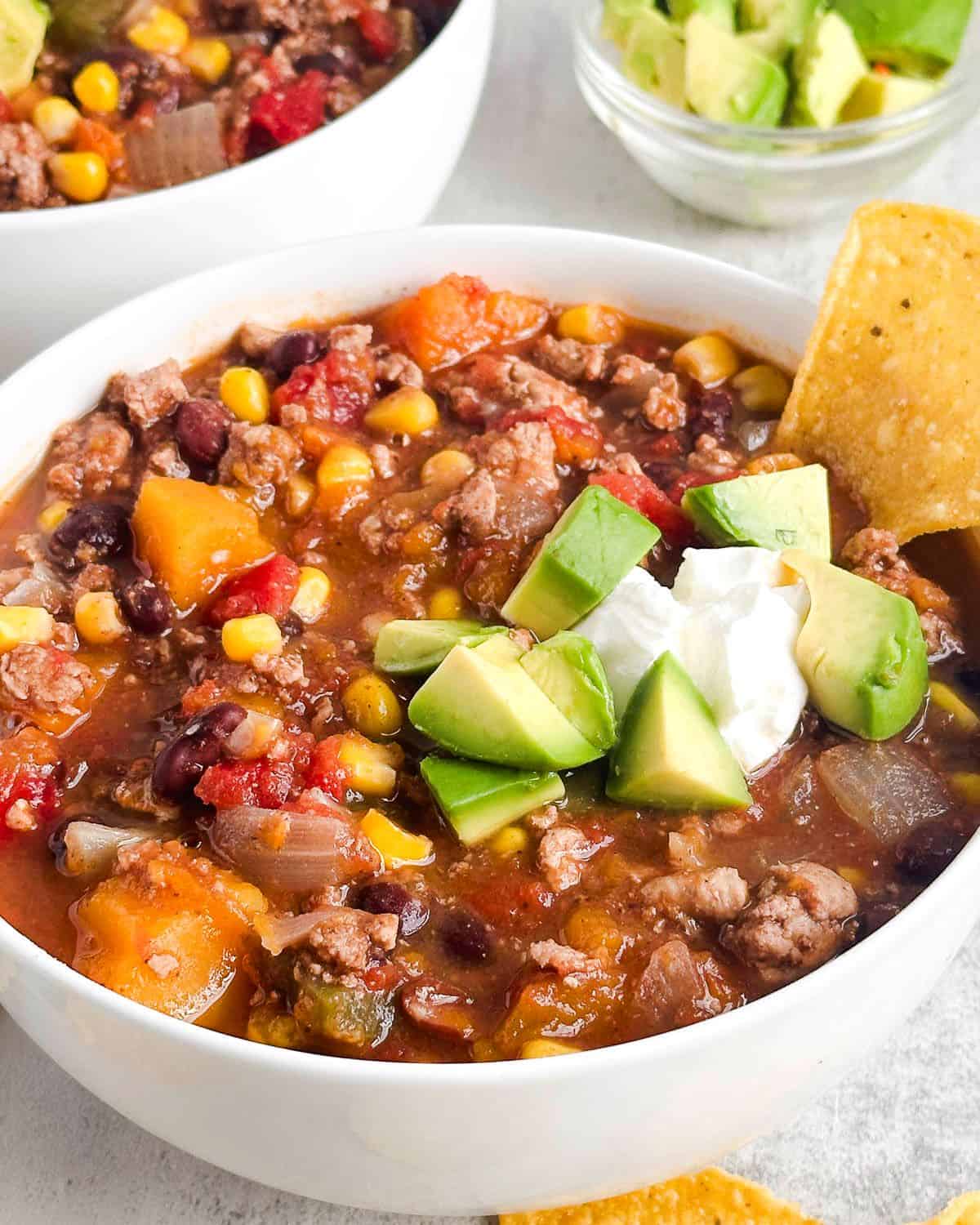 Bowls of fall harvest stye chili with sour cream, avocado, and tortilla chips.