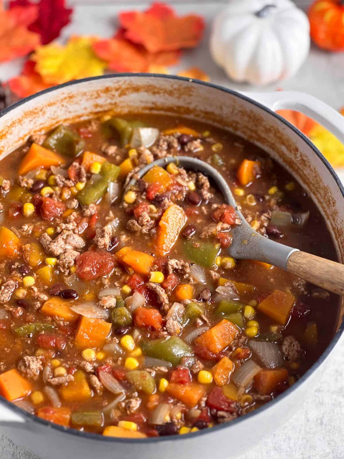 Fall harvest chili in a white Dutch oven with a serving spoon.