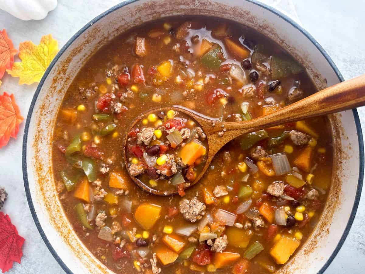 Harvest chili with fall spices in a white pot with a wooden spoon.