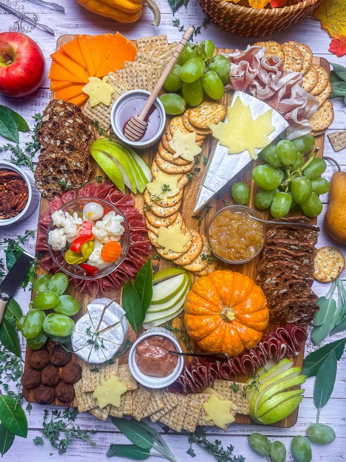 Fall themed charcuterie board display including pumpkin, pear, apple, cheese, crackers, and grapes.
