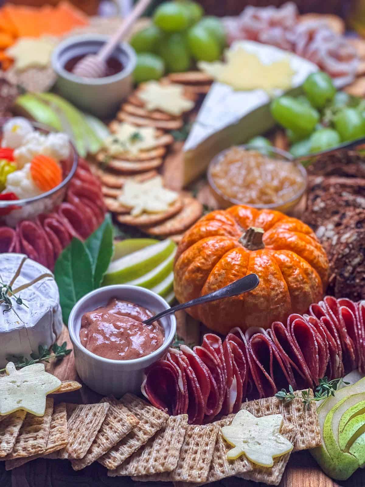 Portrait shot of the charcuterie board at 45 degree angle with cranberry mustard, crackers, cheeses, meats, and fruit in the foreground and background.