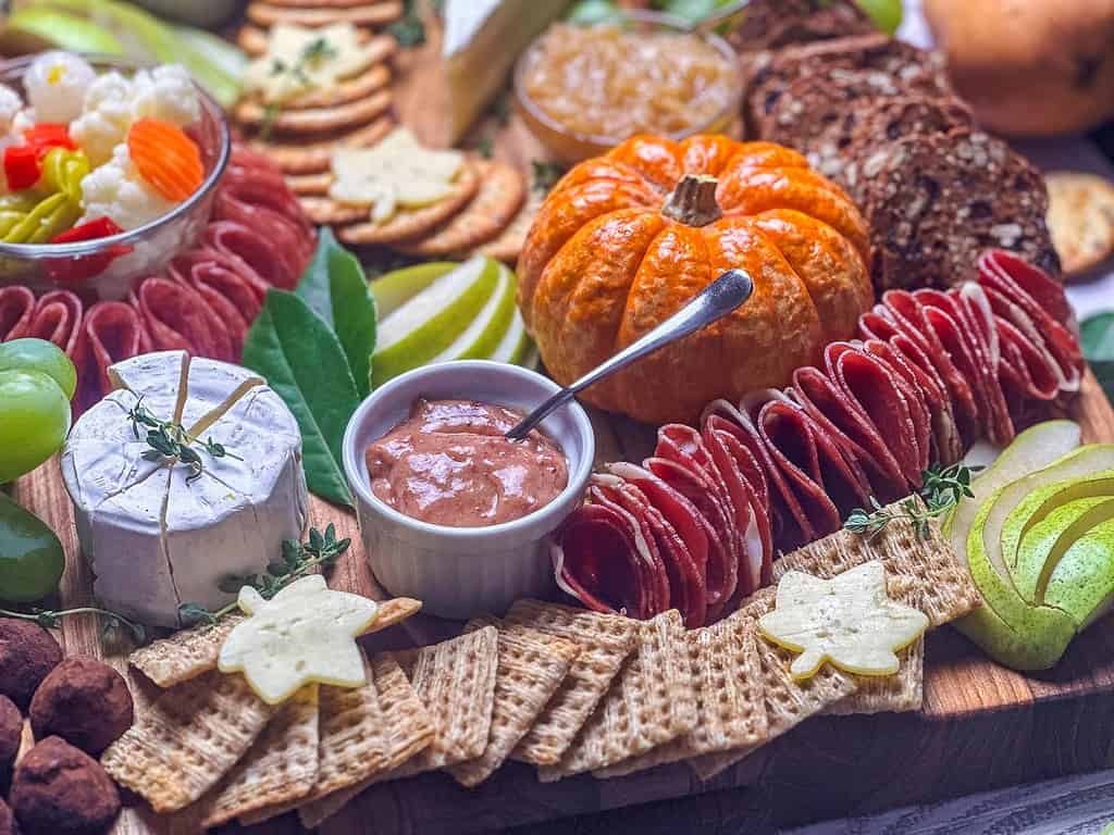 Landscape side view of the charcuterie board with cheeses, meat, a mini pumpkin, crackers, and fruit.