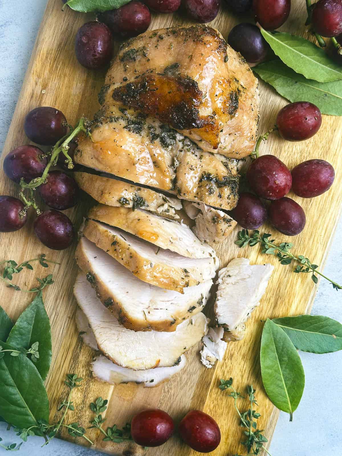 Maple bourbon glazed turkey breast on a wooden serving board with red grapes and fresh green herbs.