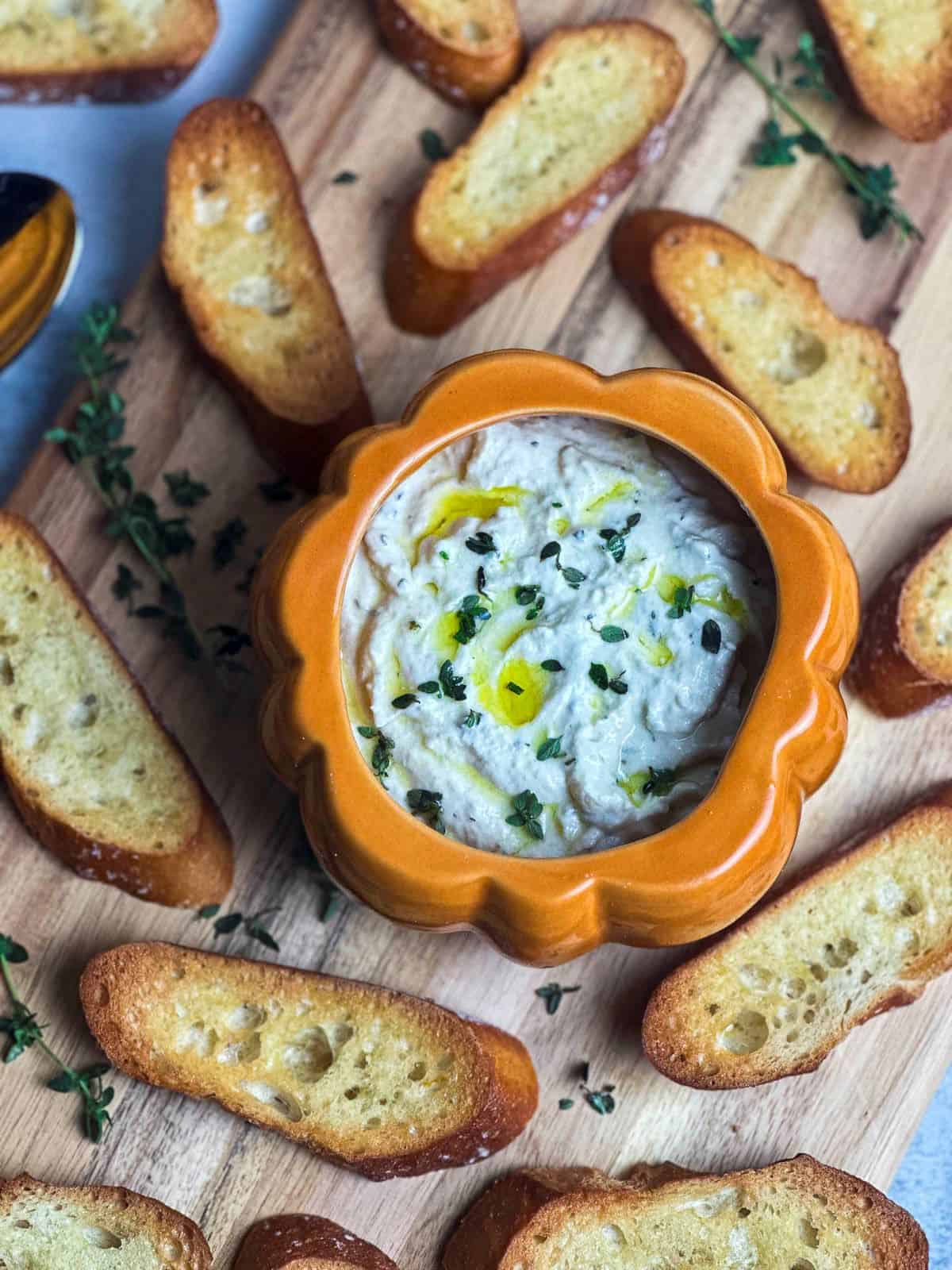 Truffle burrata dip in a pumpkin dish on a wooden board with crostini.