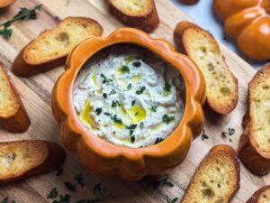 Close up shot of whipped truffle burrata dip in a pumpkin dish with drizzled olive oil and fresh thyme.