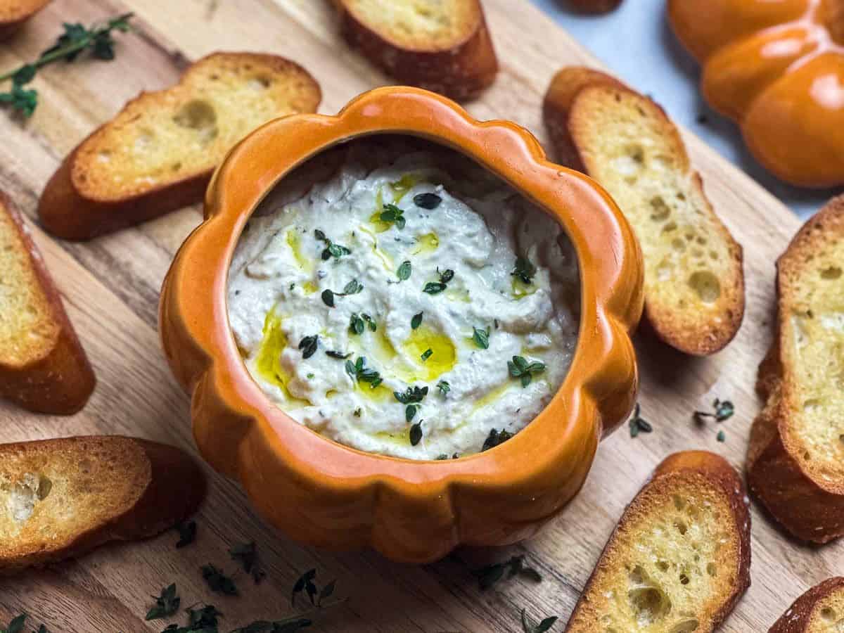 Close up shot of whipped truffle burrata dip in a pumpkin dish with drizzled olive oil and fresh thyme.