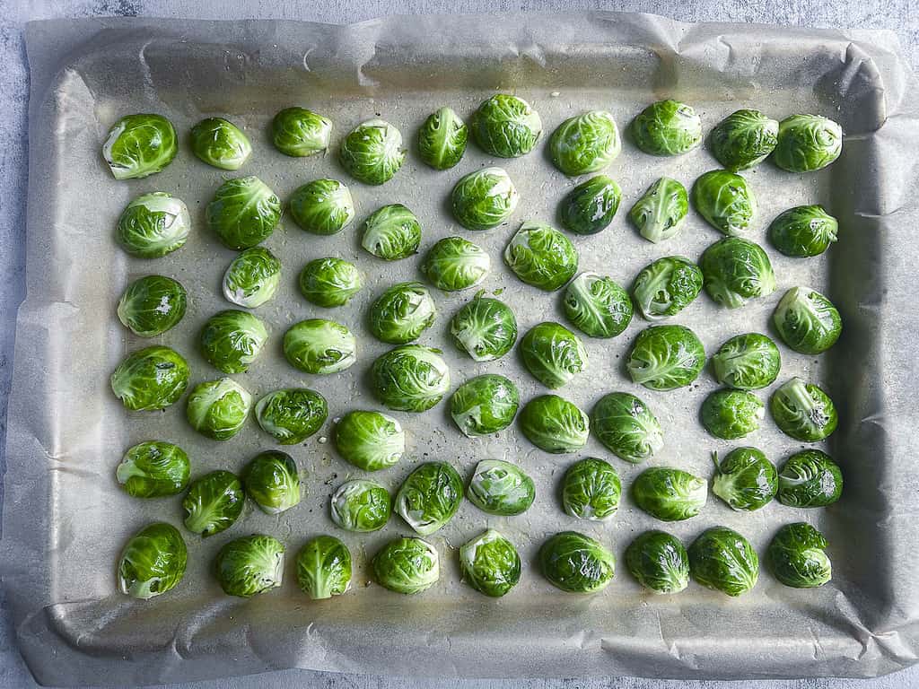 Halved Brussels sprouts spread cut side down on a parchment lined baking sheet.