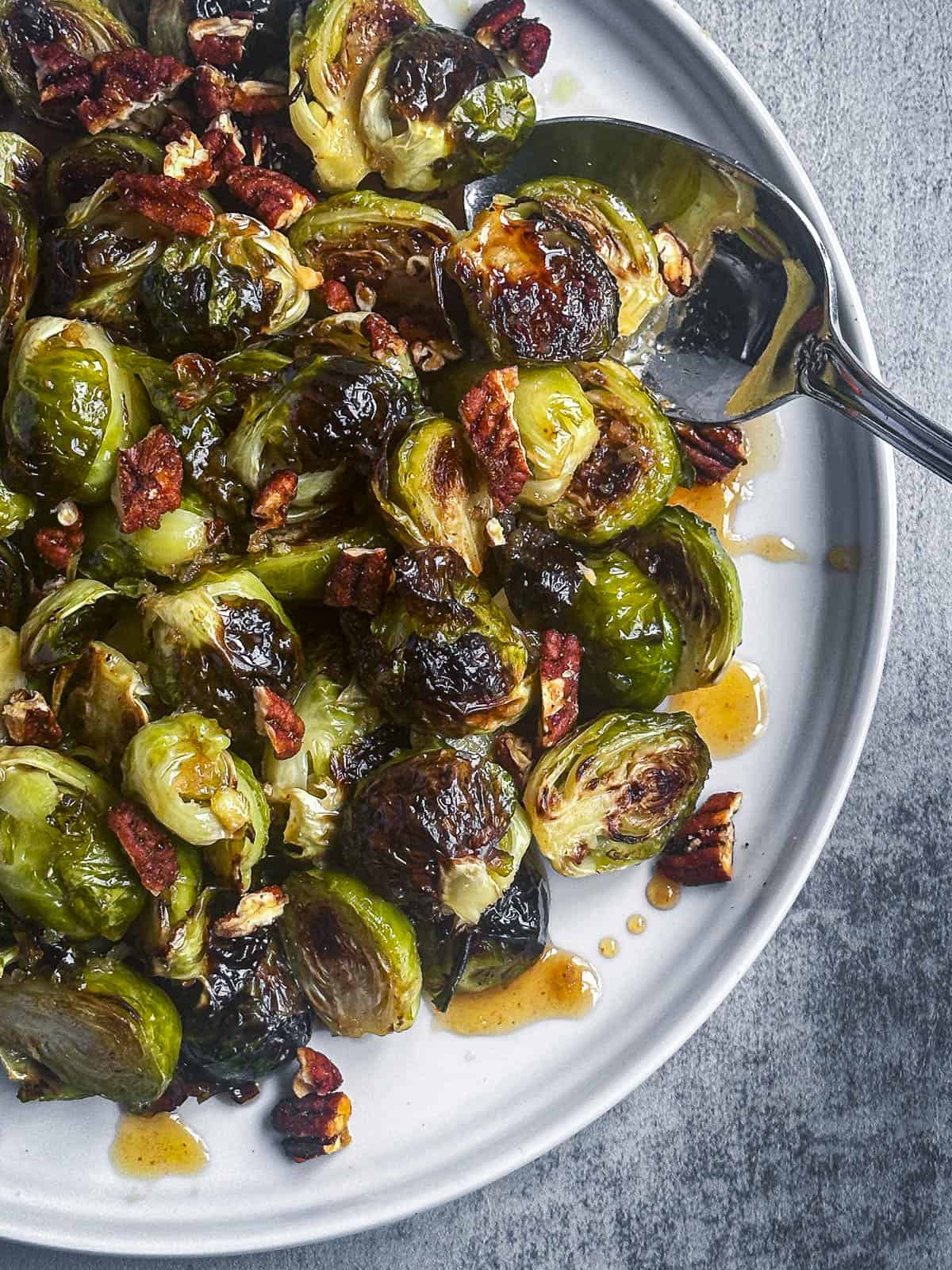 Maple sriracha glazed brussels sprouts with sweet and spicy pecans on a white plate.