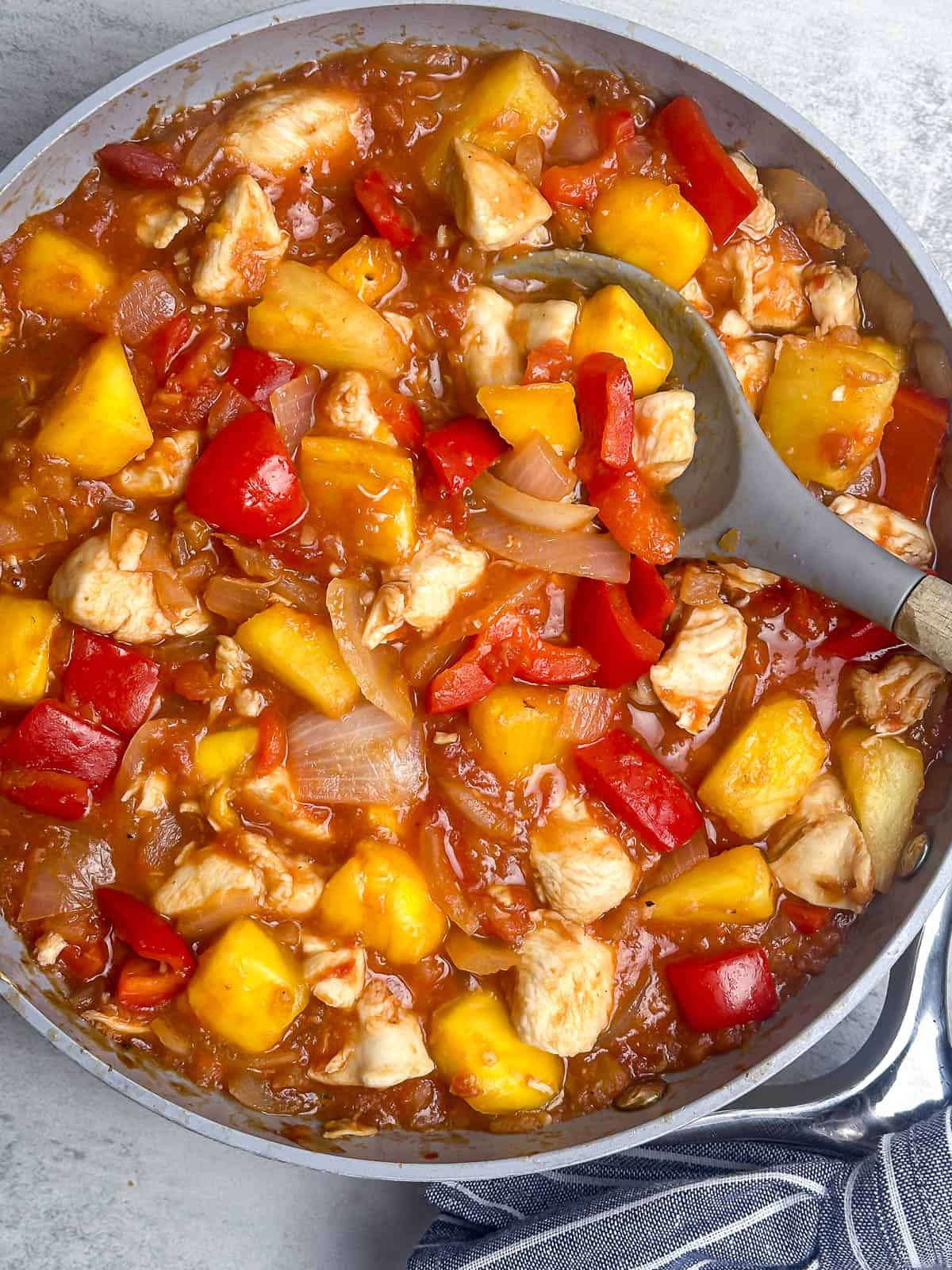 Mango pineapple salsa chicken in a skillet with a serving spoon.