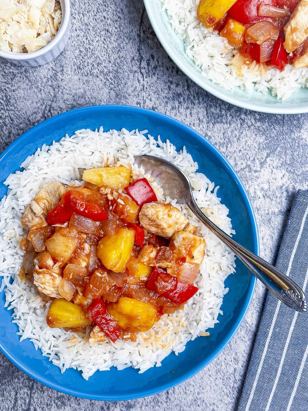 Pineapple mango salsa chicken over rice in a blue bowl with a spoon.
