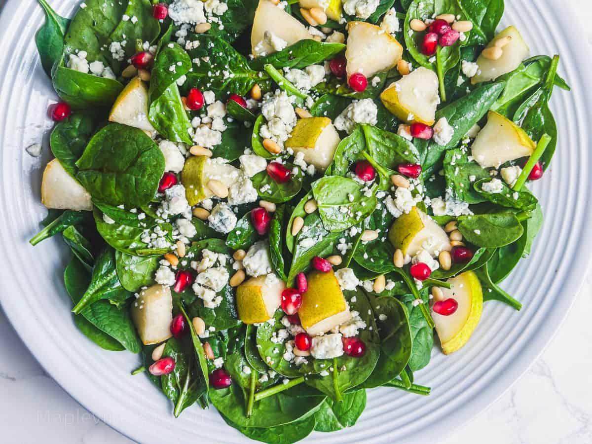 Spinach and Gorgonzola salad with pear and pomegranate in a white serving bowl.