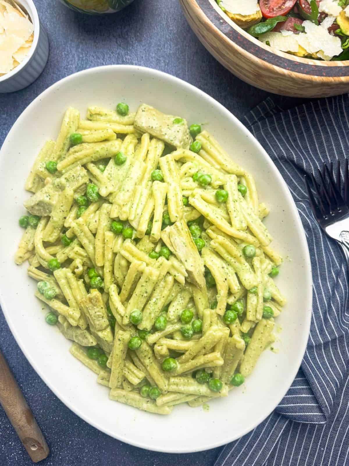 Ricotta pesto pasta with peas and artichokes on a white oval serving platter.