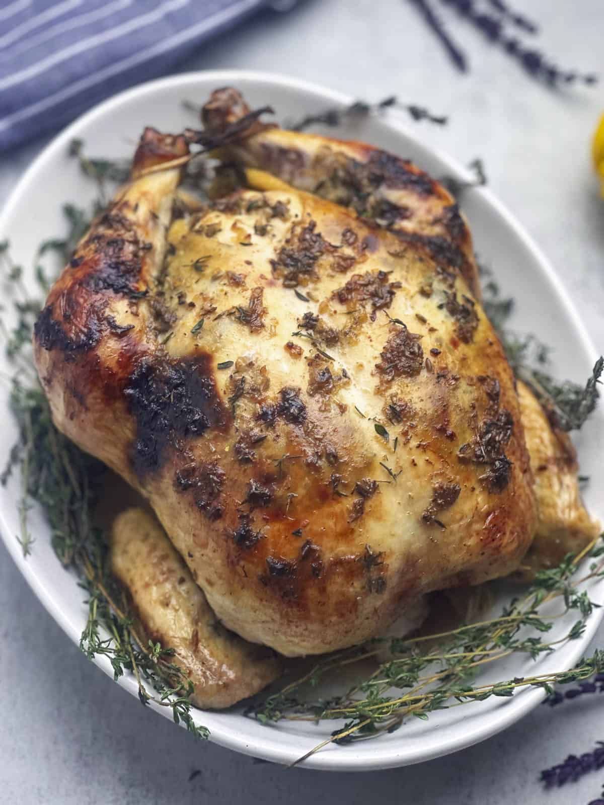 Lavender and herb butter glazed and roasted whole chicken on a serving platter with fresh sprigs of thyme.