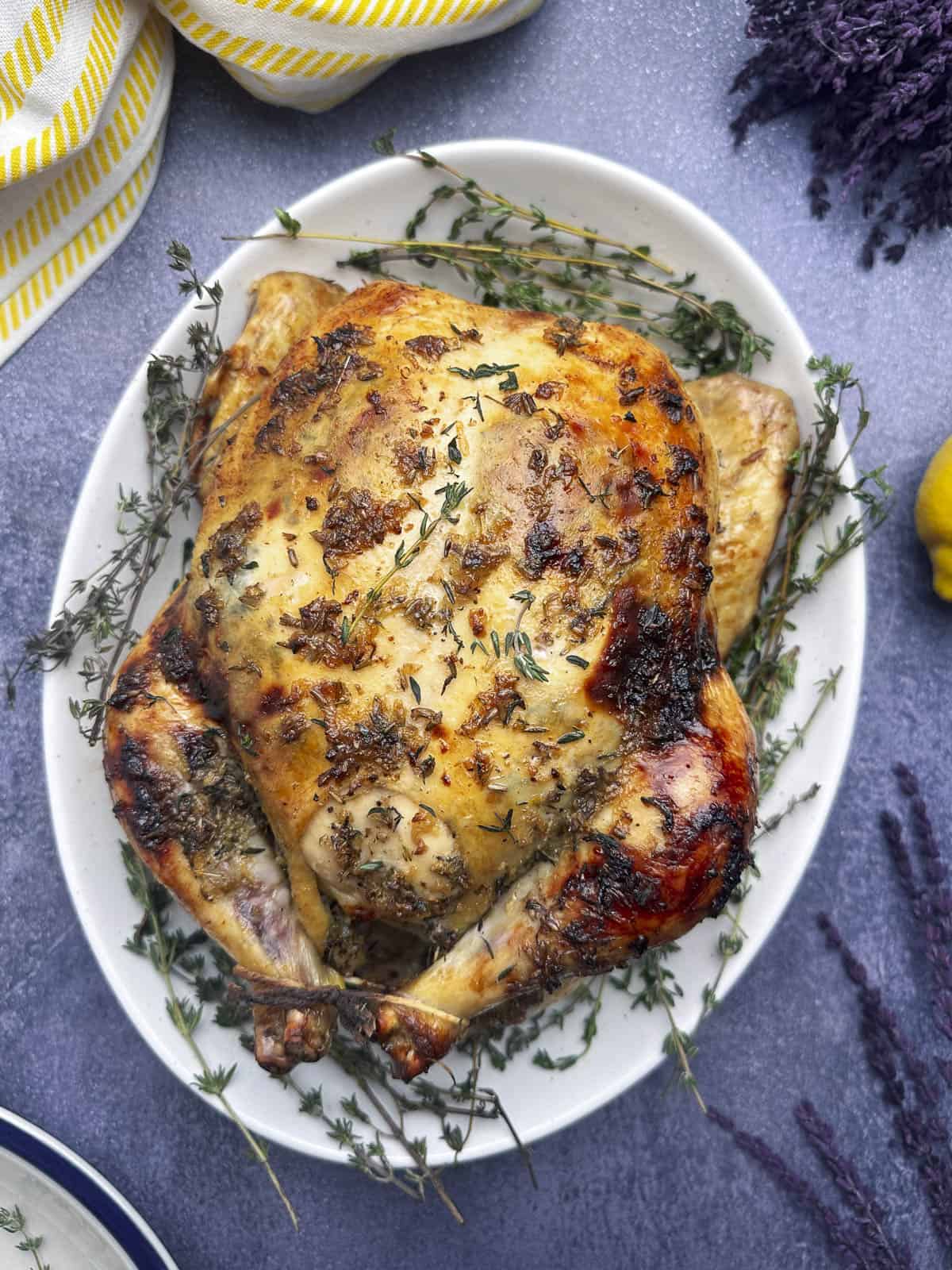 Whole roasted chicken on a serving platter with fresh thyme sprigs.