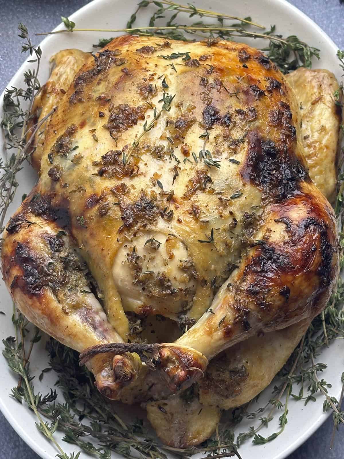 Whole roasted chicken on a white oval serving platter and surrounded by fresh thyme springs and lavender.