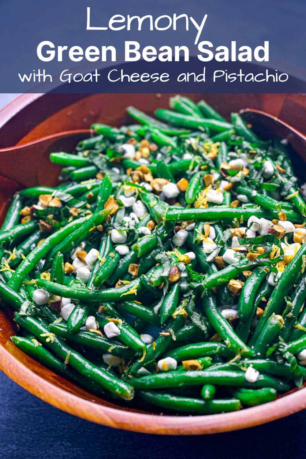 Green bean salad in a wooden bowl topped with goat cheese and pistachios.
