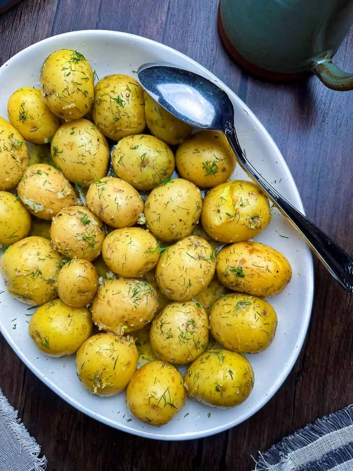 Buttered new potatoes with dill, garlic, and lemon on a white oval plate.