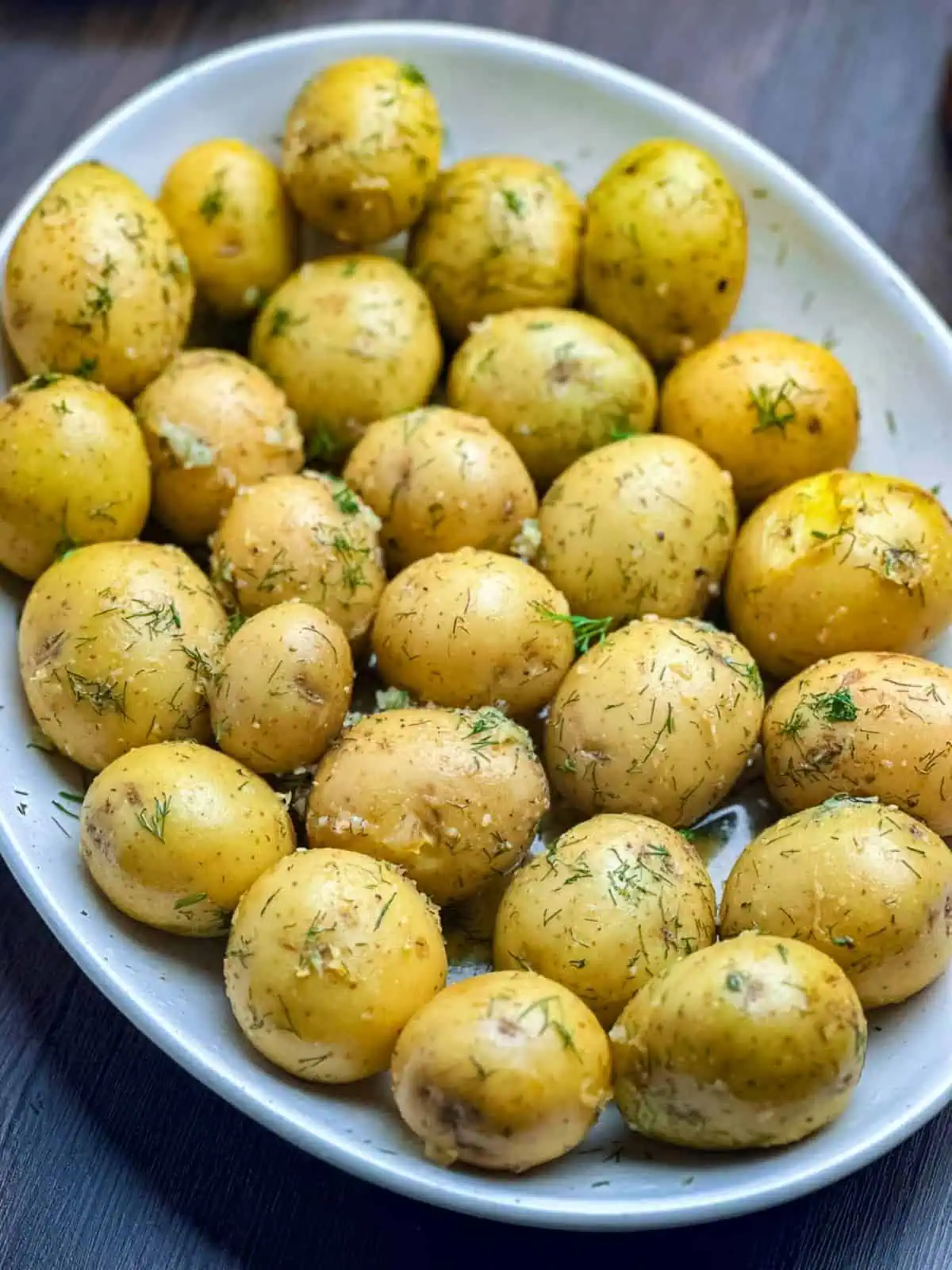 Buttered new potatoes with lemon, dill, and garlic on a white oval plate.