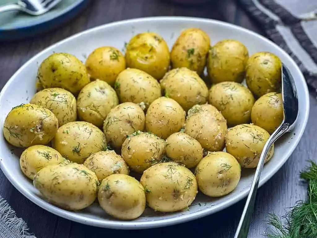 Buttered new potatoes with dill, garlic, and lemon on a white oval plate.