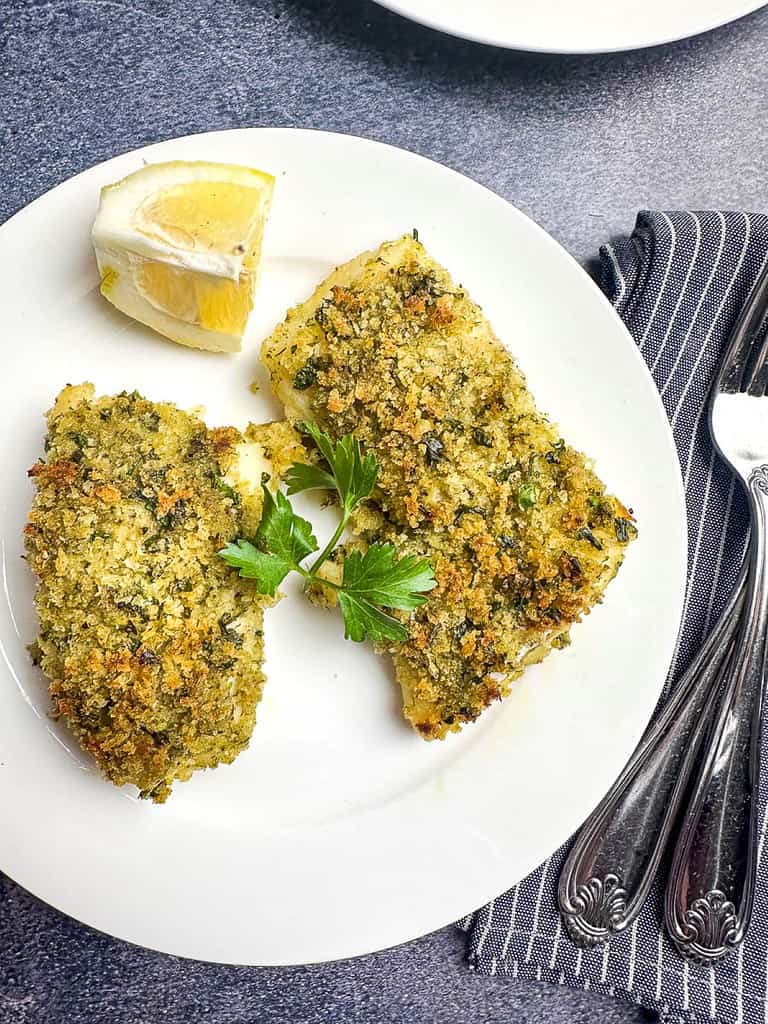 Lemon herb crusted cod fillets on a white plate with forks on the side.