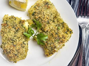 Two fillets of lemon herb crusted cod on a white plate with forks on the side.