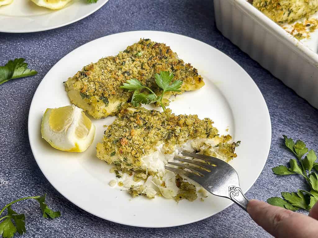 Lemon herb crusted cod on a white plate with a fork digging in.