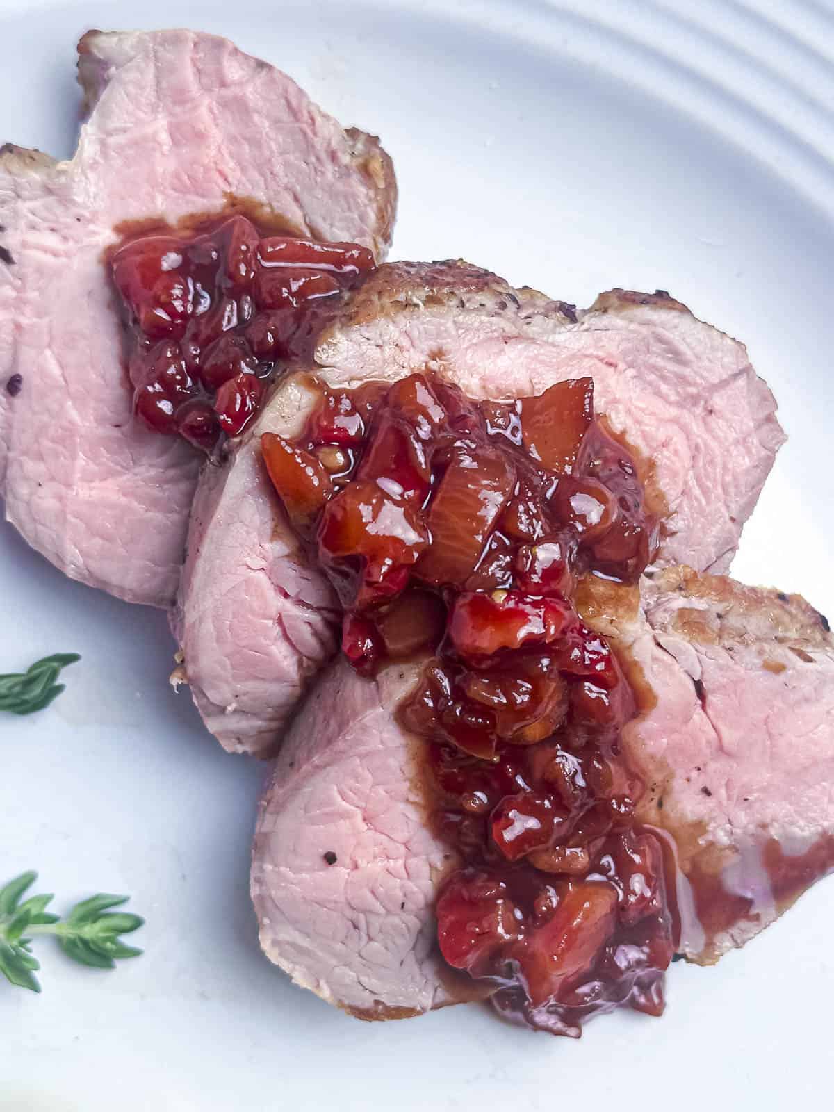 A sliced pork tenderloin with balsamic strawberry sauce on a white dinner plate.